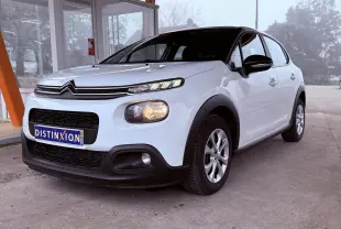 Citroën C3 blanc vue 3/4 avant droit, avec calandre noire et phares allumés sous abri.