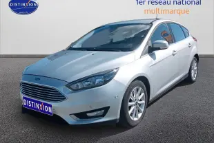 Ford Focus gris clair vue 3/4 avant droit sur parking avec calandre chromée et jantes alu