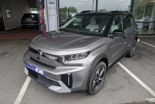Vue 3/4 avant droite d'une Citroën C3 Aircross gris Mercuy avec toit noir, garée devant un bâtiment vitré.