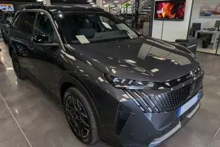 Vue 3/4 avant droit du Peugeot 5008 Hybrid gris titane avec toit noir et calandre au design moderne en concession.