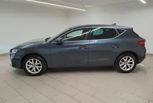 Vue de profil côté gauche d'une SEAT LEON 1.5 eTSI Hybrid gris magnétique avec vitres arrière surteintées en intérieur neutre.