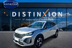 Peugeot 2008 gris artense vue 3/4 avant droit, avec jantes alu et calandre distinctive devant un showroom Distinxion.
