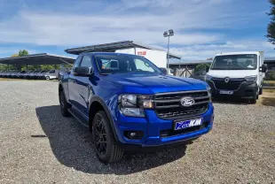 Ford Ranger Super Cabine bleu Lightning en 3/4 avant droit sur parking gravillonné, avec plaques Zero KM visibles.