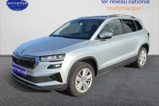 Skoda Karoq gris 3/4 avant droit, avec calandre noire et jantes alliage visibles sur sol gris.