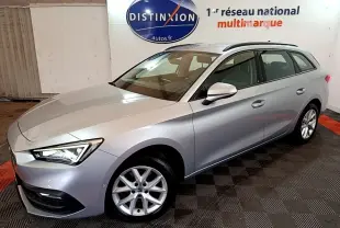 Vue 3/4 avant droit d'une SEAT Leon break gris clair avec jantes alliage et phares LED allumés en intérieur showroom.