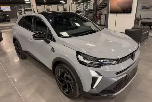 Renault Symbioz E-Tech gris Rafale en 3/4 avant droit, avec jantes noires et feux LED distinctifs, en showroom intérieur.