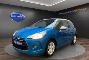Citroën DS3 e-HDi 90 bleu vue 3/4 avant droit avec toit et rétroviseurs blancs, phares allumés en showroom.