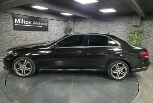 Profil côté gauche d'une Mercedes Classe E 300 BlueTEC Hybrid noire avec jantes alliage 18 pouces en intérieur showroom.