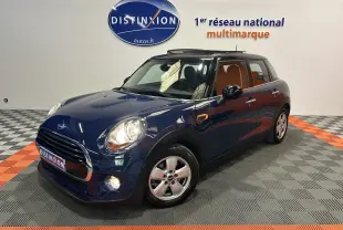 Vue 3/4 avant d'une MINI 5 portes Cooper D bleu foncé avec toit ouvrant, en intérieur sur sol damier gris et orange.