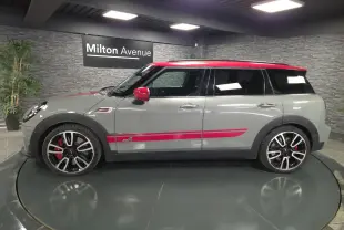 Vue de profil droit d'une MINI Clubman gris métallisé avec toit et rétroviseurs rouges, bandes décoratives sport rouges et jantes 19 pouces.