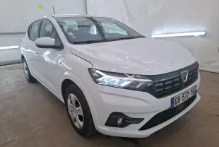 Vue 3/4 avant droite d'une Dacia Sandero III blanche de 2022 avec calandre noire et phares allumés dans un garage.