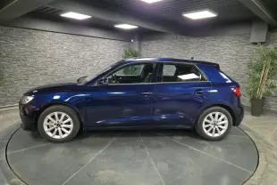 Audi A1 Sportback bleu métallisé vue de profil côté gauche dans un showroom avec sol gris et murs en pierre.
