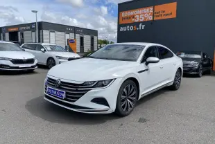 Volkswagen Arteon blanc pur vu en 3/4 avant droit sur parking devant un bâtiment commercial.