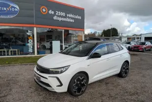 Opel Grandland blanc métallisé en 3/4 avant droit avec toit noir et jantes alliage noires sur parking.