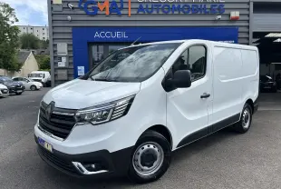 Vue 3/4 avant droit du Renault Trafic Fourgon blanc Glacier, avec calandre noire et projecteurs modernes, devant un garage.