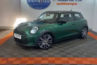 Vue 3/4 avant d'une MINI Cooper verte avec toit noir et jantes alliage, stationnée en intérieur sur sol à damiers.