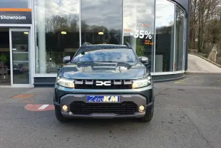 Vue frontale d'un Dacia Duster 2026 vert cèdre avec calandre noire et feux LED allumés devant un showroom.