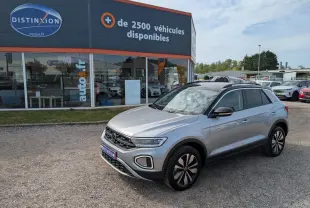 Volkswagen T-Roc gris 3/4 avant droit avec toit noir et jantes alliage 17 pouces, stationné devant un showroom.