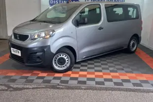 Vue 3/4 avant droit d’un Peugeot Traveller gris clair avec jantes acier et calandre noire, stationné en intérieur.