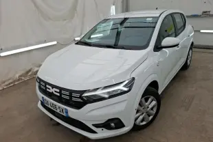 Vue 3/4 avant droit d'une Dacia Sandero blanche 2024 avec calandre noire et feux LED allumés dans un garage.