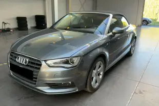 Audi A3 Cabriolet gris vue 3/4 avant droit avec capote noire dans un garage lumineux.