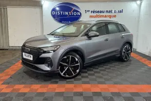 Audi Q4 E-TRON gris foncé en 3/4 avant droit, avec jantes noires et détails noirs brillants visibles en intérieur showroom.