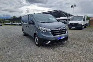Renault Trafic Fourgon gris Highland en 3/4 avant droit sur parking gravillonné, avec calandre chromée et feux LED.