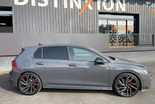 Profil côté gauche d'une Volkswagen Golf VIII GTI gris métallisé avec jantes noires à détails argentés et étriers rouges.