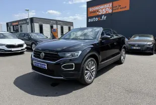 Volkswagen T-Roc Cabriolet noir nacré en 3/4 avant droit sur parking avec jantes alliage et capote ouverte.