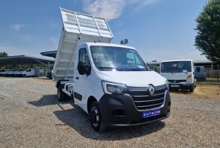 Renault Master Benne blanc vu 3/4 avant droit, benne relevée et roues jumelées visibles sur terrain gravillonné.