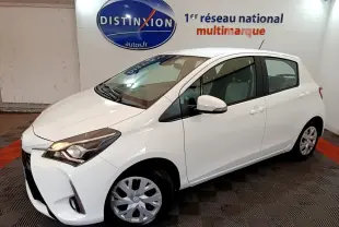 Toyota Yaris blanche vue 3/4 avant droit, avec phares allumés et jantes en alliage visibles.