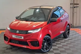 Vue 3/4 avant d'une Aixam Ambition rouge 2025 avec toit noir et jantes noires brillantes dans un intérieur neutre.