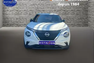 Vue frontale d'un Nissan Juke blanc 2024 avec calandre noire et phares ronds distinctifs sur fond de mur en briques.