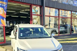 Vue 3/4 avant d'une Dacia Sandero III blanche glacier garée devant un garage avec logo AD Expert visible.