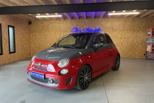 Vue 3/4 avant droite de l'Abarth 500 rouge avec capot noir et jantes noires à rayons fins dans un showroom.