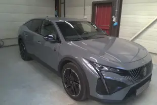Peugeot 408 HYBRID 145 GT gris Selenium vue 3/4 avant droit, avec calandre distinctive et jantes noires.