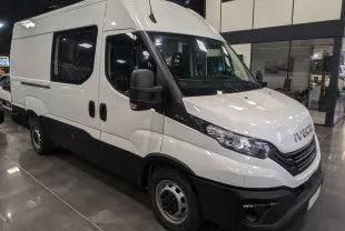 Fourgon Iveco Daily blanc vu en 3/4 avant droit dans un showroom avec vitres teintées et pare-chocs noirs.