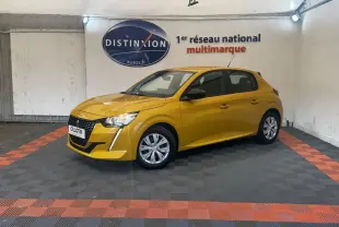 Peugeot 208 jaune vue 3/4 avant droit, avec calandre noire et feux LED, stationnée en intérieur sur sol damier noir et orange.