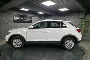 Profil côté gauche d'un Volkswagen T-Roc blanc 2022 avec jantes alliage et toit noir en showroom.
