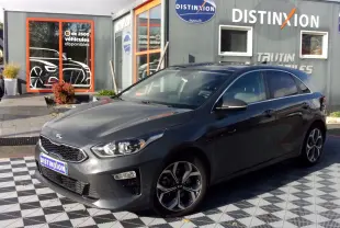 KIA CEE'D gris vue 3/4 avant droit, avec jantes alliage et calandre noire, stationnée devant un showroom Distinxion.