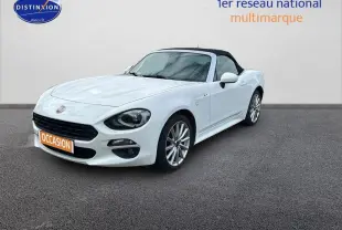 Fiat 124 Spider blanc vue 3/4 avant avec capote noire et jantes alliage 17 pouces sur sol gris.
