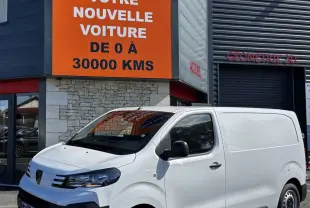 Peugeot Expert Fourgon blanc en 3/4 avant droit, stationné devant un bâtiment commercial avec panneau orange.