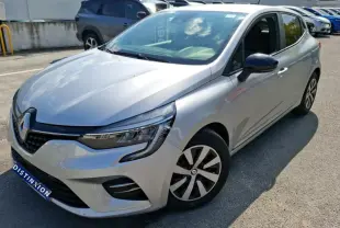 Renault Clio gris clair vue 3/4 avant droit, avec jantes spécifiques et calandre moderne, stationnée en extérieur.