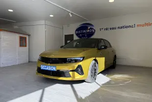 Opel Astra jaune vue 3/4 avant droit en intérieur, avec calandre noire et jantes foncées, plaque "OCCASION" visible.