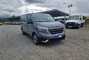 Renault Trafic Fourgon gris urbain vu en 3/4 avant droit sur un parking avec plusieurs véhicules utilitaires.