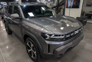 Dacia Duster gris schiste en 3/4 avant droit, avec calandre moderne et jantes noires bicolores en showroom.