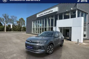 Volkswagen Tiguan gris en 3/4 avant droit, avec jantes alliage noir brillant, devant un bâtiment de concession.