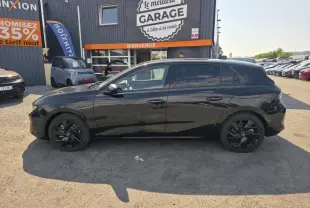 Opel Astra Hybrid 2024 noir profil côté gauche avec jantes alliage noires et vitres surteintées, stationnée devant un garage.