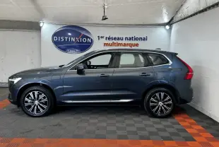 Profil droit d’un Volvo XC60 bleu hybride rechargeable avec jantes alliage et rails de toit chromés, en intérieur showroom.