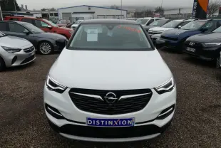 Vue avant d'un Opel Grandland blanc avec calandre noire et phares LED, sur un parking de voitures.